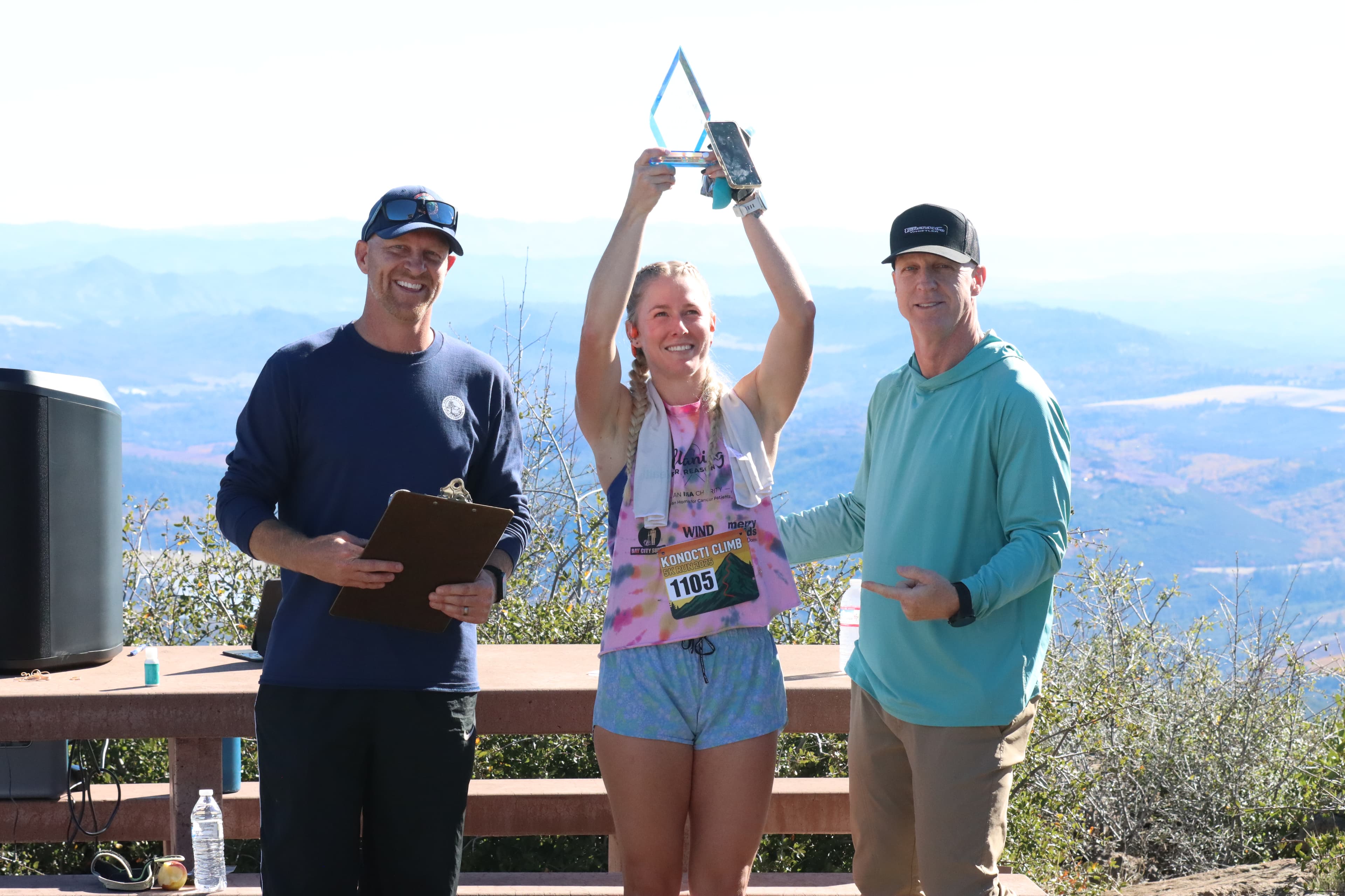 The 2025 Queen of the Mountain raising a trophy at the summit awards celebration.