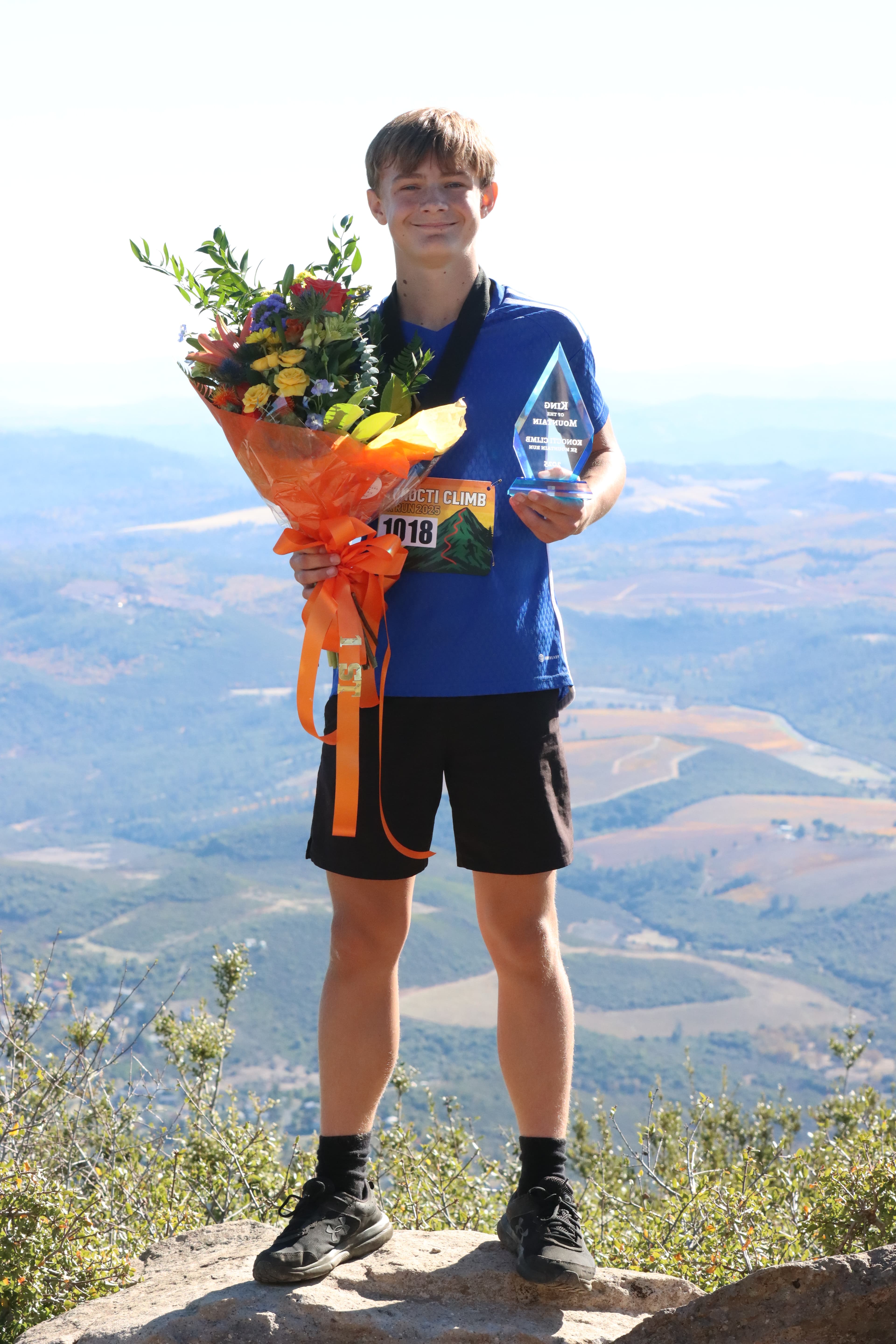 The 2025 King of the Mountain holding a trophy and flowers above Clear Lake.
